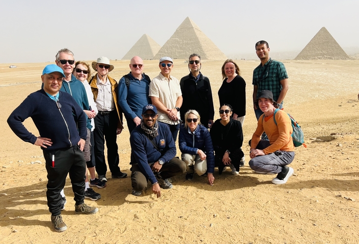       Group of tourists posing in front of pyramids.
  