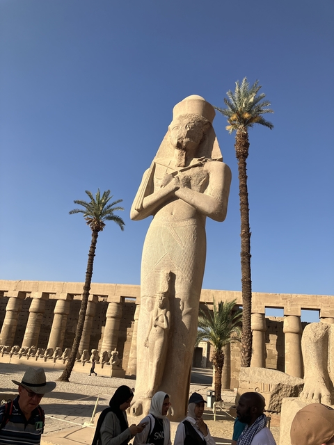       Tall ancient statue surrounded by palm trees under a clear sky.
  