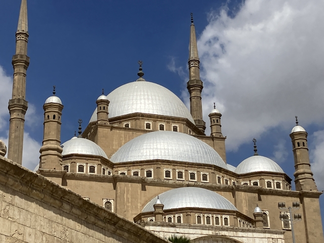       Majestic view of a mosque with multiple domes against a blue sky.
  