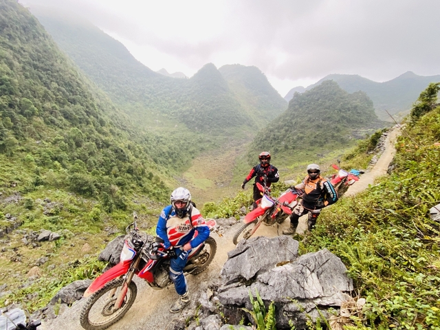 Three motorcyclists on a mountain road surrounded by lush valleys.