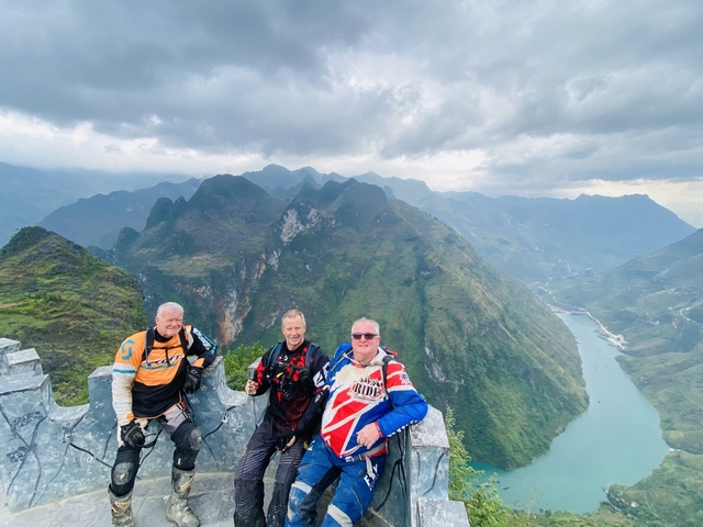 Three people in motorcycle gear posing with dramatic mountain scenery.