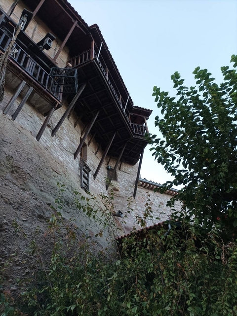 Stone building with wooden balconies and leafy branches.