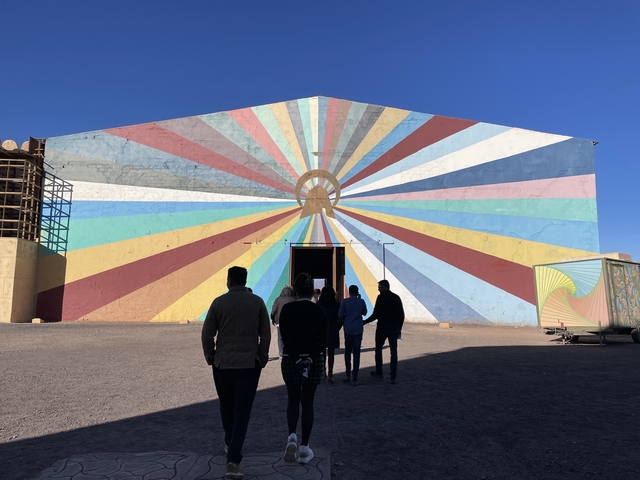       People approaching a colorful building with striped mural designs.
  
