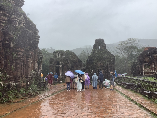 Visitors with umbrellas walking among ancient ruins.