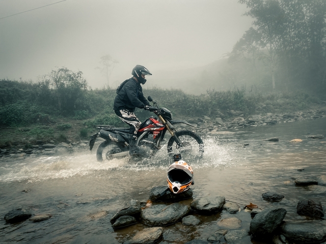 Person on a motorbike crossing a stream in a foggy landscape.