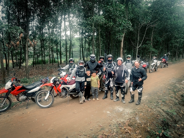 Off-road motorcyclists in a forest path posing with children.