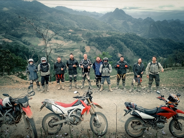 Group of motorcyclists on a scenic overlook with muddy bikes.