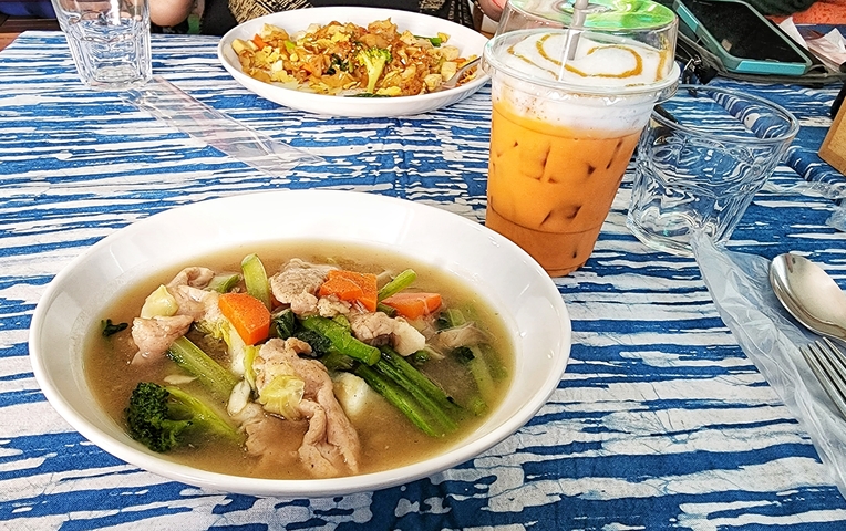       Thai meal with soup, vegetables, and iced tea.
  