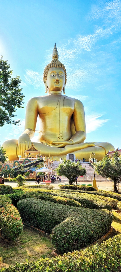       Large golden Buddha statue outdoors with visitors.
  