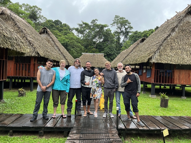       Group photo with people standing between traditional huts.
  