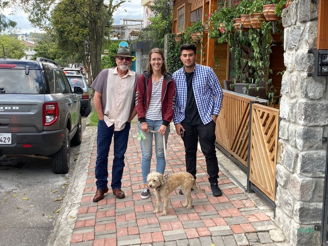       Three people and a dog on a paved sidewalk.
  