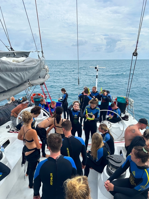 People in wetsuits on a boat at sea.
