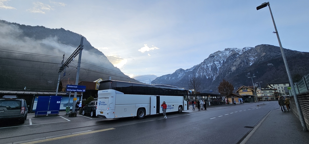       A bus parked next to a train station with mountains in the background.
  