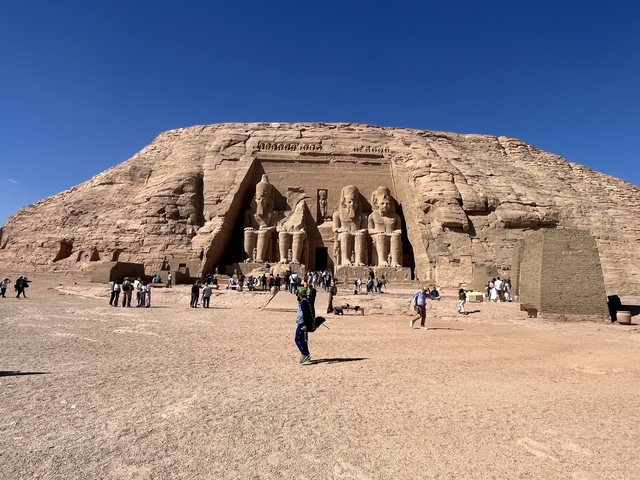       Large stone facade of a temple with statues, people in foreground.
  