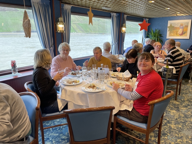 Group of people dining at a table in a restaurant with a river view.