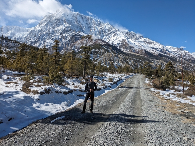 A person walking along a snowy road with large mountains in the background.