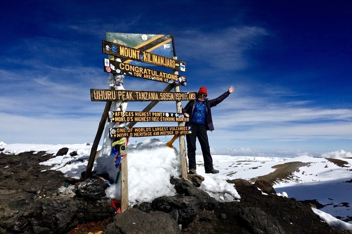 Person smiling by the Mount Kilimanjaro summit sign.