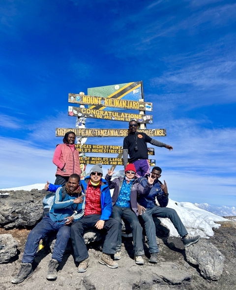 Group of people posing at the summit of Mount Kilimanjaro.