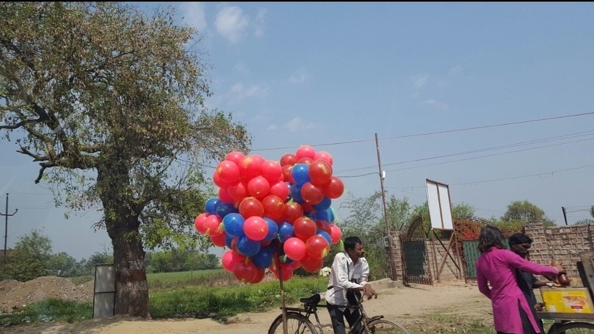 Man with balloons on a bicycle, street scene with people.
