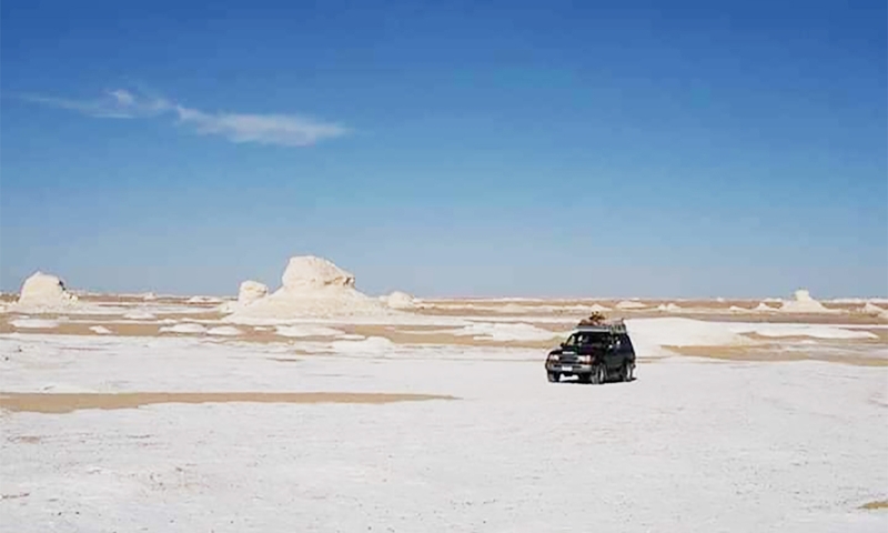 A car driving through a desert landscape with white rock formations.