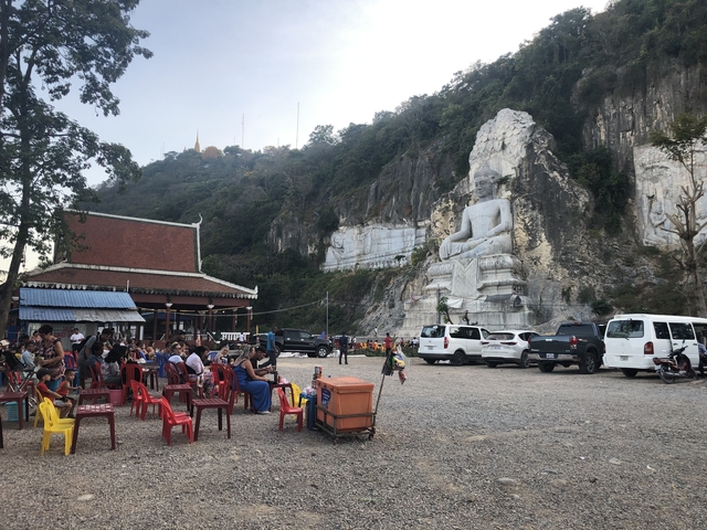 Outdoor gathering area with people seated and a large statue in the background.