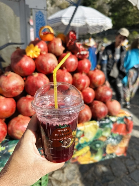       A refreshing pomegranate juice in a clear cup with a straw, in front of pomegranate fruits.
  