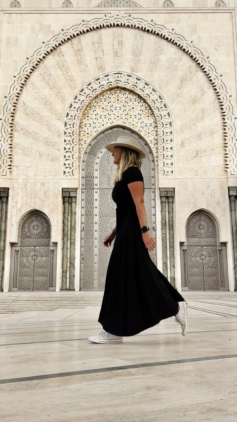       A woman in a hat strolling in front of an intricately designed archway.
  
