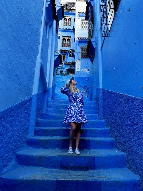       A woman posing in a vibrant blue alley with stairs.
  