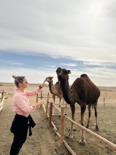       A woman interacting with two camels in a desert setting.
  