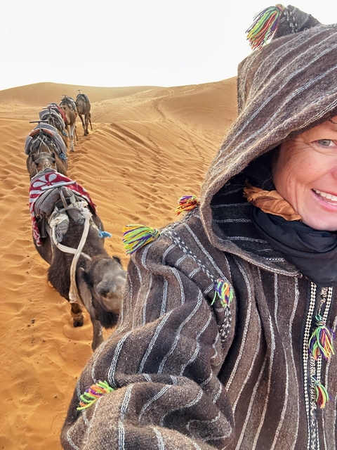       A person taking a selfie with camels in the desert.
  
