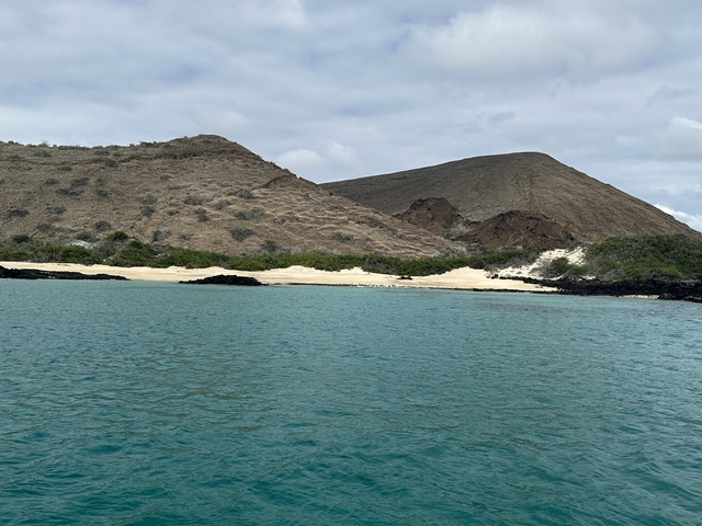       Rocky hills and calm blue sea under a cloudy sky.
  