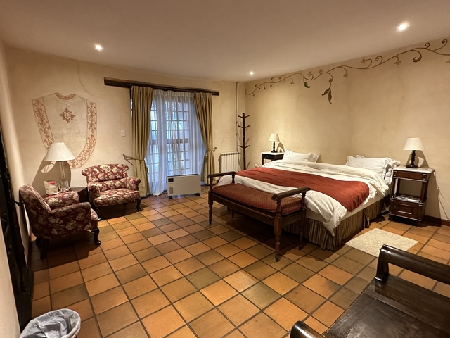       A cozy hotel room with a double bed, two chairs, and a window.
  