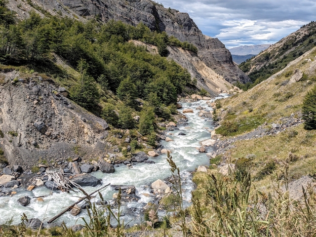       Raging river cutting through mountainous landscape with forested slopes.
  