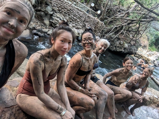 Group of people covered in mud sitting by a river.