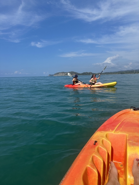       Two people kayaking in the ocean with shoreline visible.
  