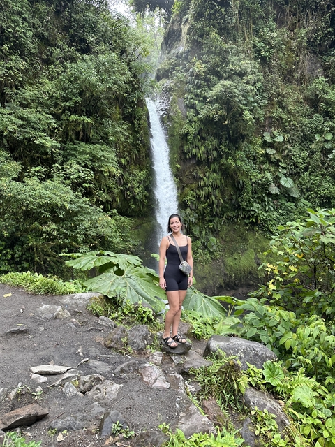      Woman posing in front of a lush green waterfall.
  