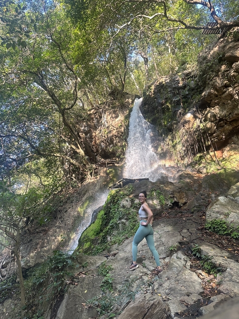 Person standing by a large waterfall in a forest setting.