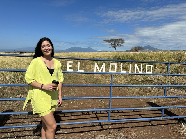 Woman smiling next to a fence with mountains in the background.