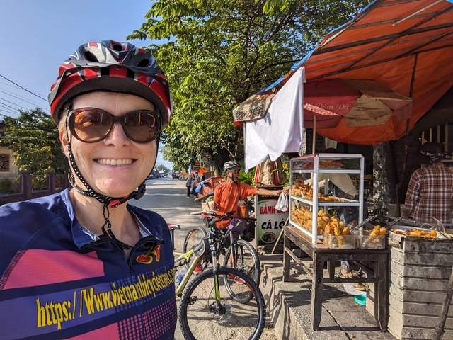 Person smiling near a street food stall with bicycles in the background.