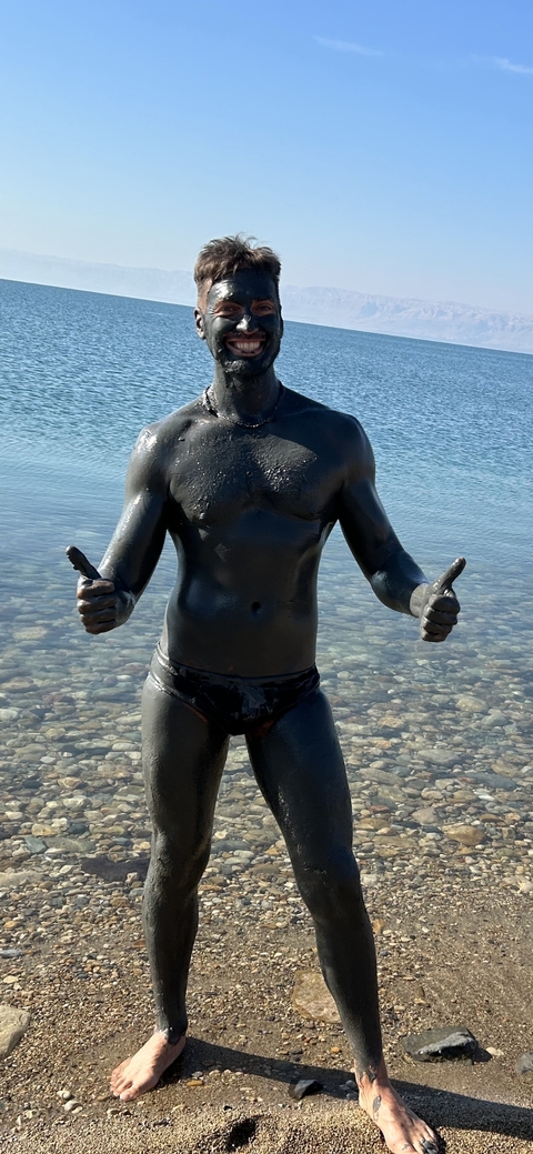       Person covered in mud giving thumbs up by the water.
  