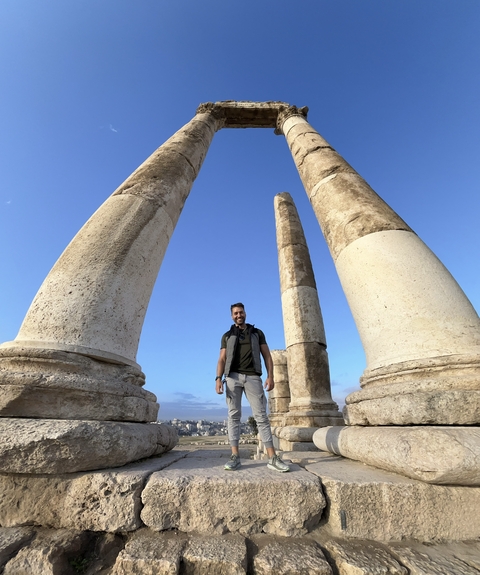 Person standing between ancient columns against blue sky