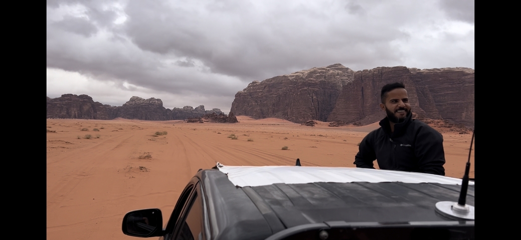       Man standing by a vehicle in a desert landscape.
  