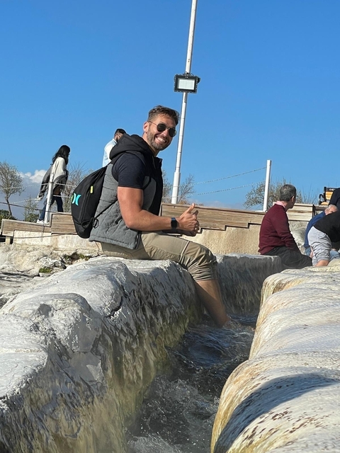 Person sitting by thermal pools with people in the background