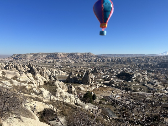      Wide landscape view of rock formations and a hot air balloon in Cappadocia.
  