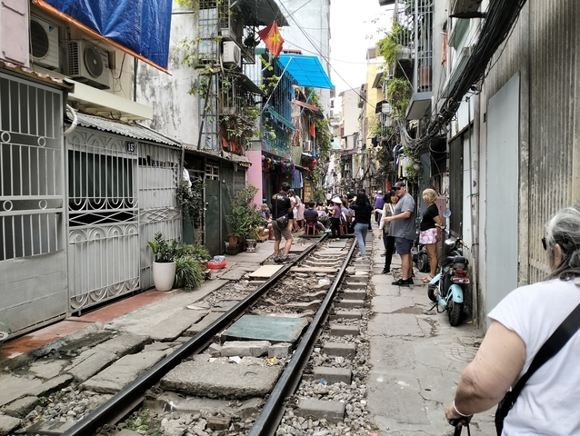       Tourists exploring a narrow street with train tracks.
  