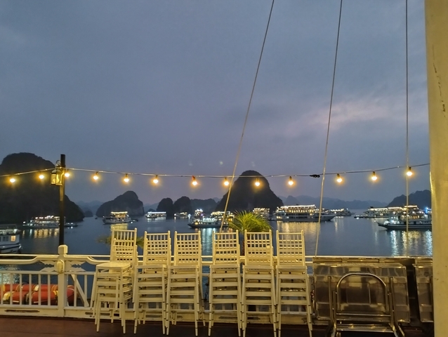       Boats and karst formations in a bay at dusk with string lights.
  