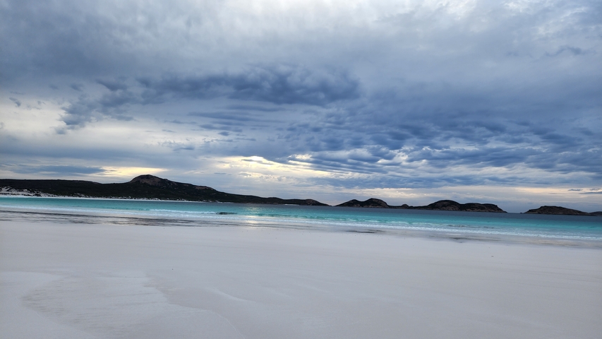 Beautiful beach with white sands and turquoise water under a dramatic sky.
