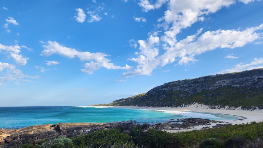 Vibrant beach scene with rocky cliffs and clear blue skies.