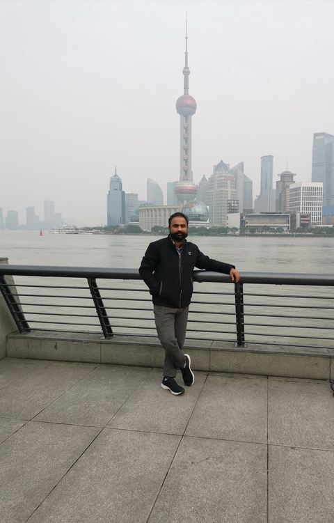 Person standing by a riverside with a cityscape in the background.