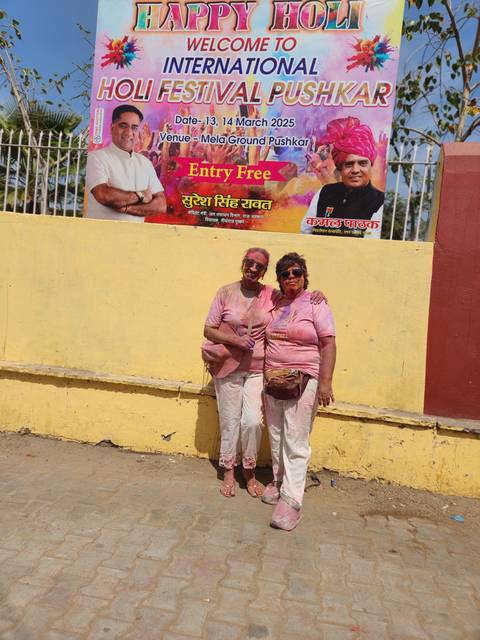People covered in colored powder standing in front of a festival banner.
